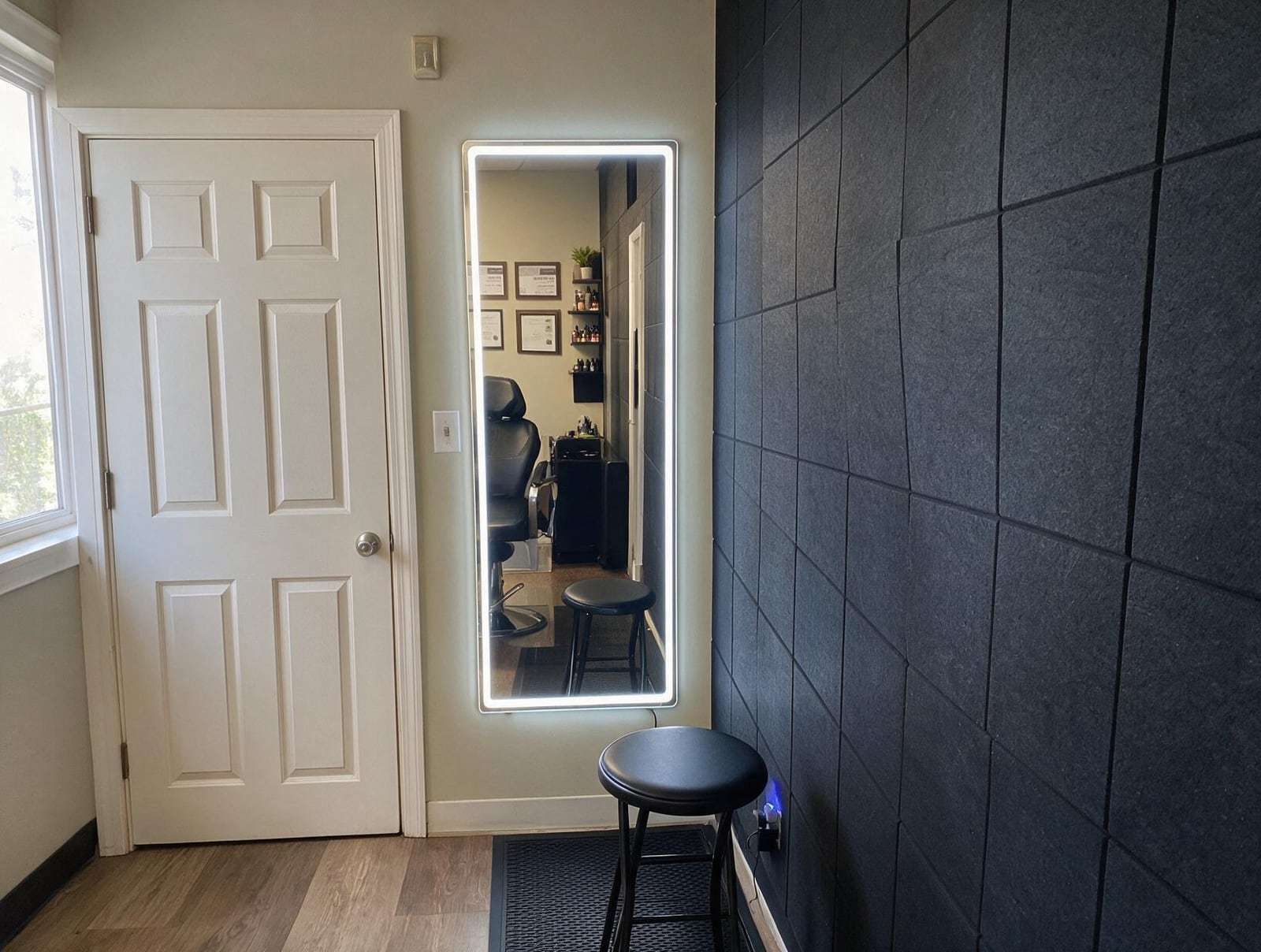 Empty treatment room with a lit full-length mirror on a cream wall, a white panelled door